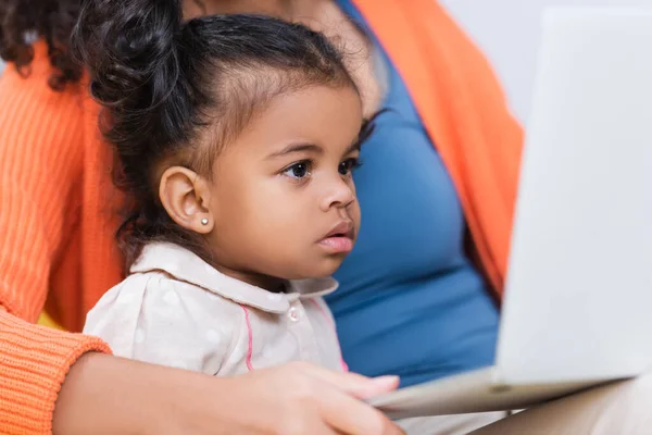 Afro-américaine pigiste en utilisant un ordinateur portable près de la fille tout-petit à la maison — Photo de stock