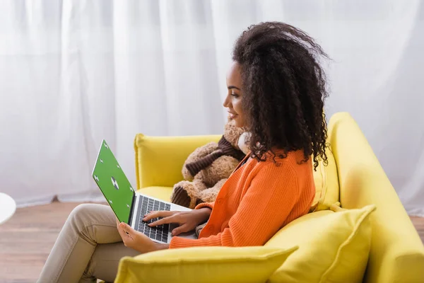 Vista lateral do feliz freelancer afro-americano usando laptop com tela verde em casa — Fotografia de Stock