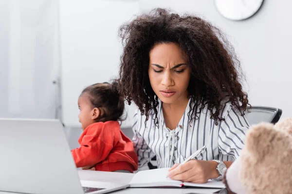 Stressed african american mother holding in arms crying toddler daughter while working from home — Stock Photo