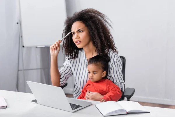 Pensativo africano americano madre sentado con niño hija mientras trabajo desde casa — Stock Photo