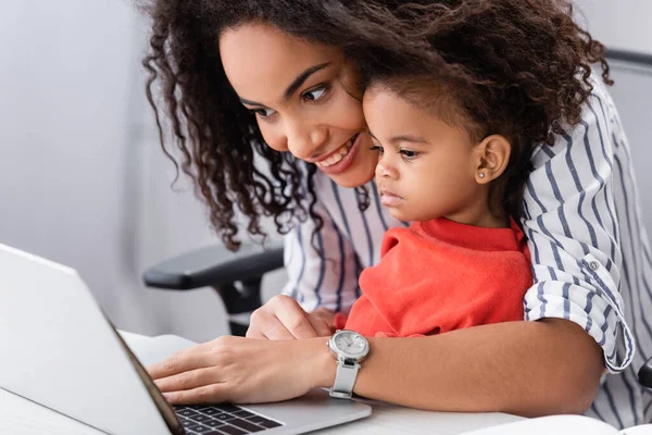 Счастливая африканская американская мать смотрит на ноутбук с дочерью малыша — стоковое фото