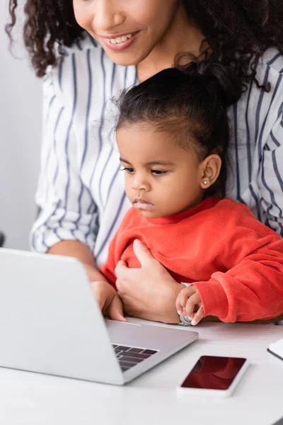 Африканская американская мать сидит с малышом дочь и с помощью ноутбука на столе — стоковое фото