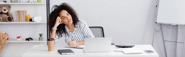 Pensive african american woman writing in notebook near gadgets on desk, banner — Stock Photo