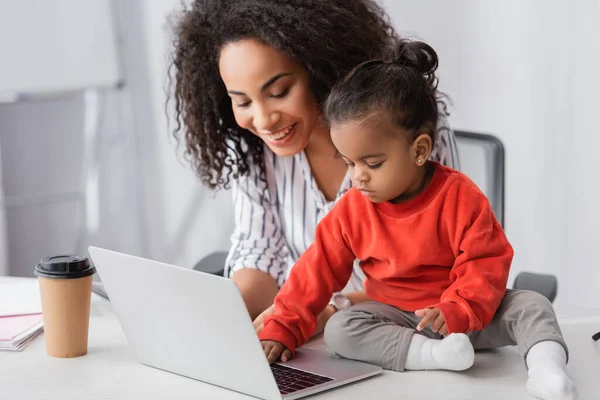 Toddler african american child typing on laptop near cheerful mother — Stock Photo