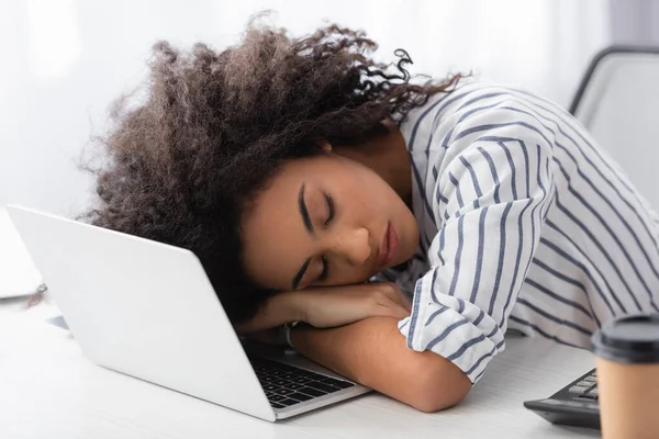 Mujer afroamericana agotada durmiendo en el ordenador portátil en casa - foto de stock