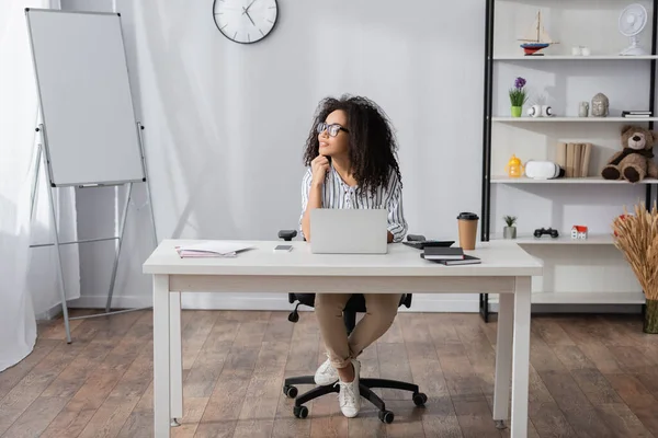 Freelancer afroamericano en gafas mirando hacia otro lado mientras trabaja desde casa - foto de stock