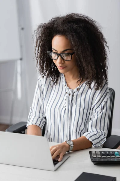 Freelancer afro-americano em óculos digitando no laptop enquanto trabalhava em casa — Fotografia de Stock