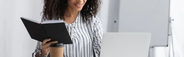 Vue partielle de joyeux freelance afro-américain tenant carnet tout en travaillant de la maison, bannière — Photo de stock