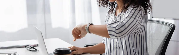 Vue partielle de pigiste afro-américain regardant la montre près d'un ordinateur portable à la maison, bannière — Photo de stock
