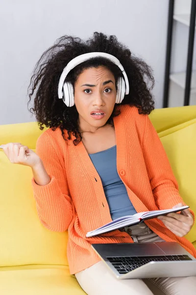 Afro-américaine femme tenant carnet et écoute podcast dans les écouteurs — Photo de stock