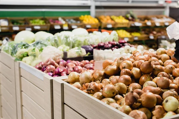 Cebollas frescas y verduras sobre fondo borroso en el supermercado - foto de stock