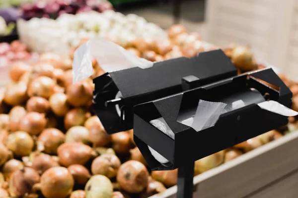 Stand avec des emballages en plastique près des oignons sur fond flou dans les supermarchés — Photo de stock