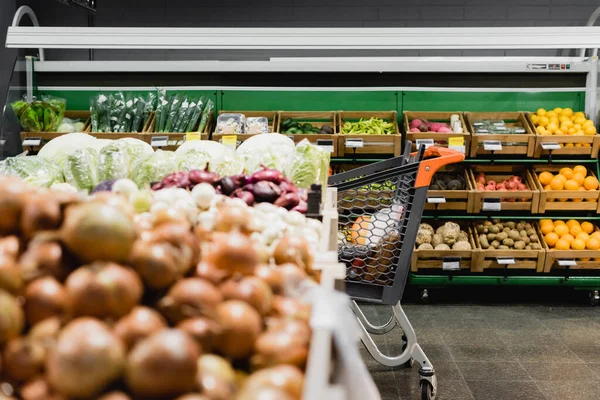 Shopping trolley near vegetables on blurred foreground in supermarket — Stock Photo