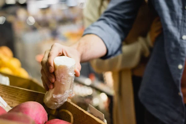 Vista ritagliata dell'uomo che tiene il ravanello vicino alla ragazza su sfondo sfocato nel supermercato — Foto stock