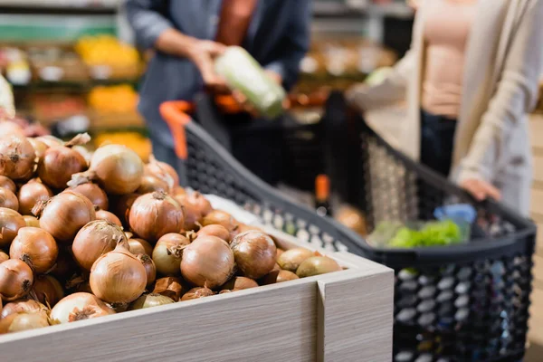 Ausgeschnittene Ansicht von Zwiebeln in der Nähe von Paar auf verschwommenem Hintergrund im Supermarkt — Stockfoto