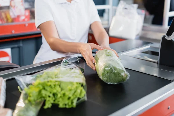 Cropped view of cashier taking lettuce from supermarket checkout — Stock Photo