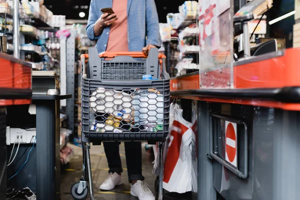 Cropped view of man using smartphone while standing near shopping cart on supermarket checkout — Stock Photo