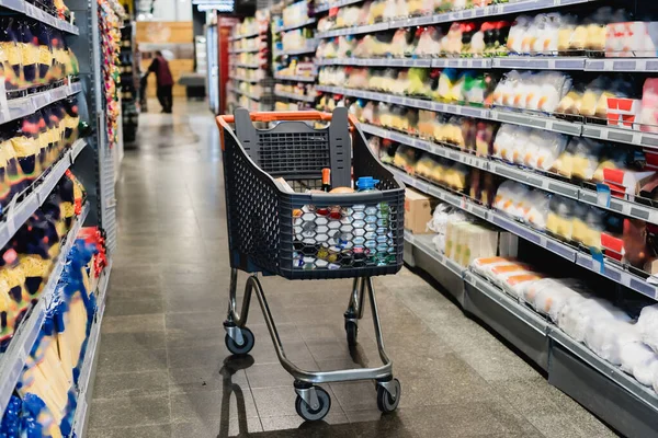 Shopping trolley near shelves with groceries in supermarket — Stock Photo
