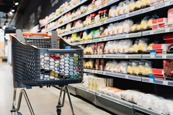 Einkaufswagen in der Nähe von Paketen in den Regalen im Supermarkt — Stockfoto