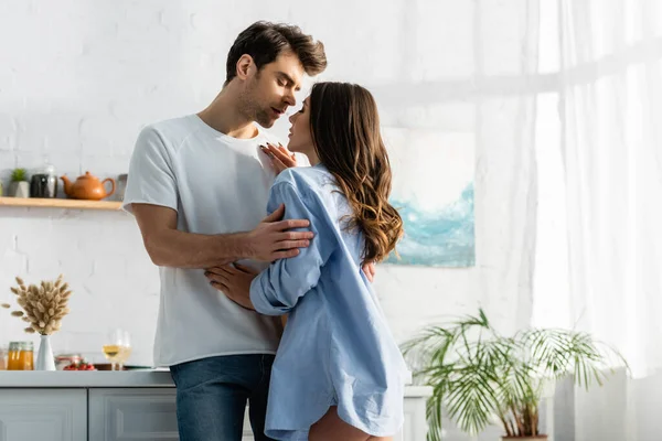 Homem abraçando mulher sensual em camisa azul na cozinha — Fotografia de Stock