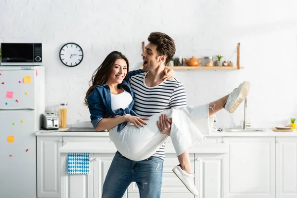 Erstaunter Mann hält lächelnde Freundin in der Küche in den Armen — Stockfoto