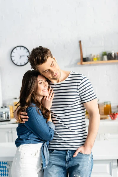 Man hugging cheerful girlfriend and looking away in kitchen — Stock Photo