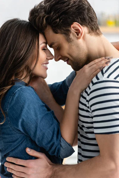 Vista lateral de pareja alegre con los ojos cerrados abrazándose en la cocina - foto de stock