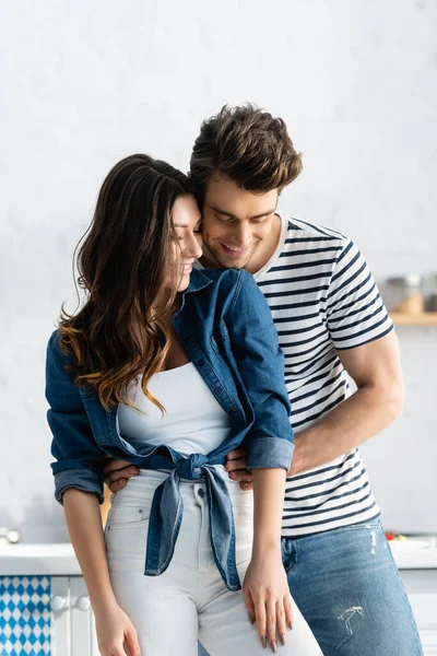 Glücklicher Mann umarmt Freundin und lächelt in Küche — Stockfoto