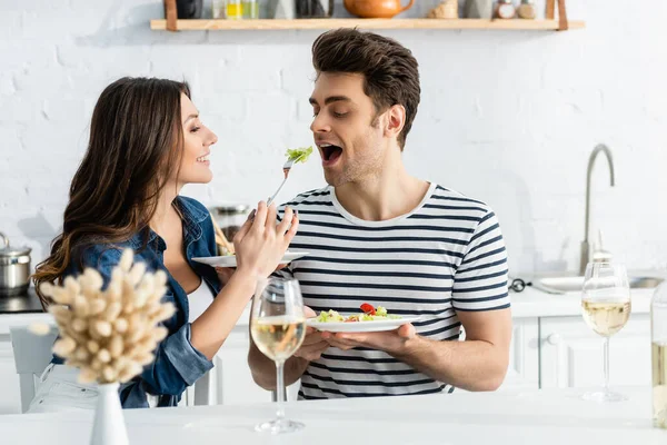 Mujer feliz sosteniendo plato y alimentando novio con lechuga - foto de stock