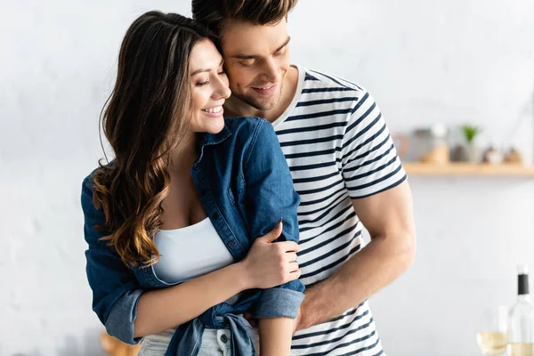 Feliz hombre abrazando alegre novia y sonriendo en la cocina - foto de stock