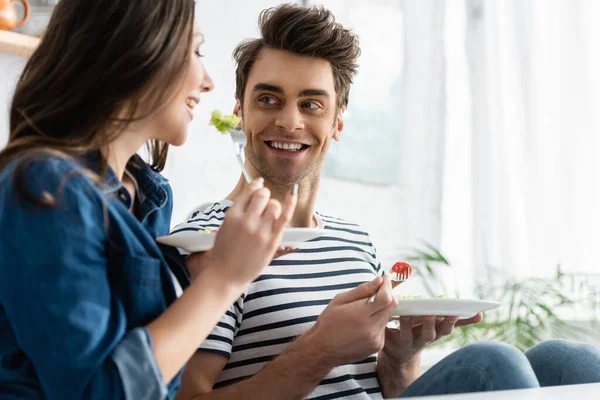 Allegro uomo che tiene piatto con insalata e guardando la ragazza in primo piano sfocato — Foto stock