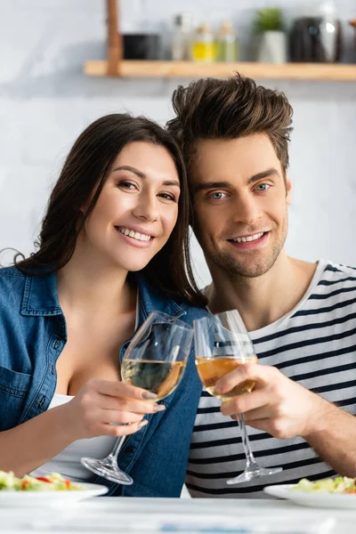 Alegre pareja tostando vasos de vino en la cocina - foto de stock