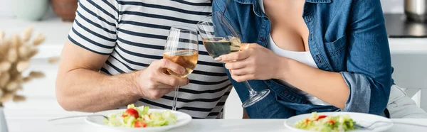 Teilansicht des Paares beim Anstoßen von Weingläsern in der Nähe von Tellern mit Salat in der Küche, Banner — Stockfoto