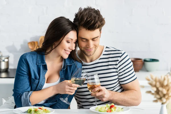 Happy couple toasting glasses of wine near plates with salad in kitchen — Stock Photo
