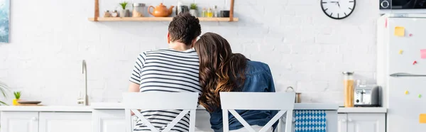 Vista trasera del hombre y la mujer sentados en sillas en la cocina, pancarta - foto de stock