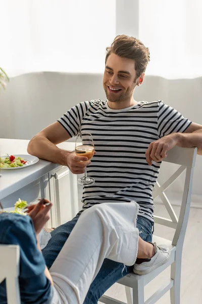 Felice uomo in possesso di un bicchiere di vino e guardando la donna in cucina — Foto stock