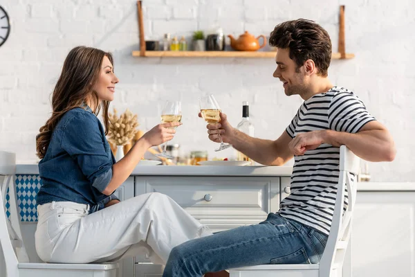 Seitenansicht eines glücklichen Paares, das in der Küche Gläser mit Wein hält — Stockfoto