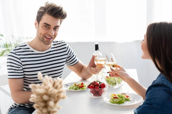 Alegre hombre y mujer tostando vasos de vino cerca del almuerzo en la mesa - foto de stock