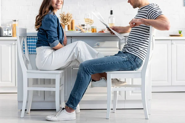 Cropped view of man sitting on chair and reading newspaper near cheerful woman — Stock Photo