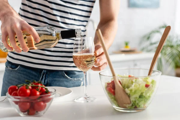 Cropped view of man pouring white wine in glass near salad — Stock Photo