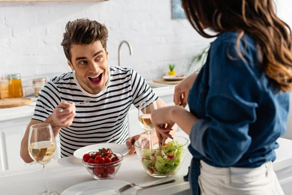 Verblüffter Mann schaut Frau beim Servieren von Salat in Küche auf verschwommenem Vordergrund an — Stockfoto