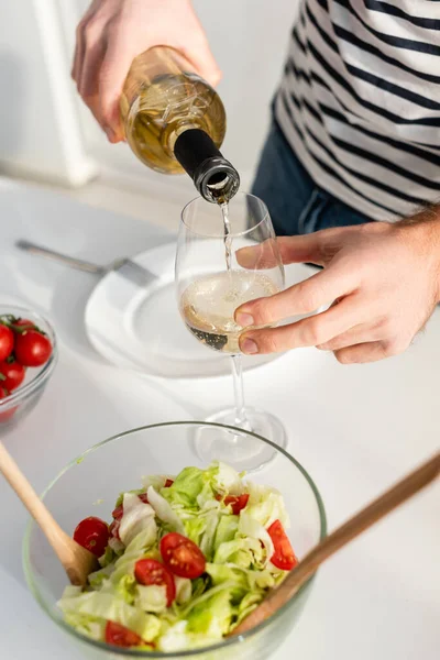 Partial view of man pouring white wine in glass near fresh salad — Stock Photo