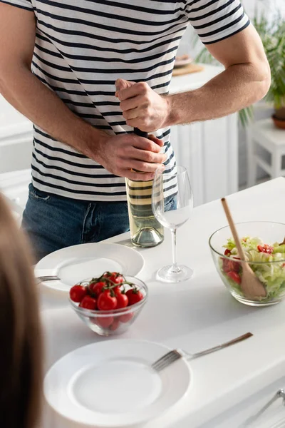 Vista cortada do homem que abre a garrafa no vinho perto da mulher em primeiro plano borrado — Fotografia de Stock