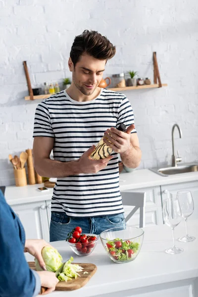 Hombre feliz sonriendo mientras mira la botella de vino en la cocina - foto de stock