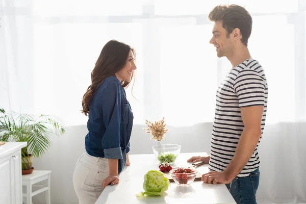 Seitenansicht eines glücklichen Paares, das sich in der Nähe von Zutaten auf dem Tisch anschaut — Stockfoto
