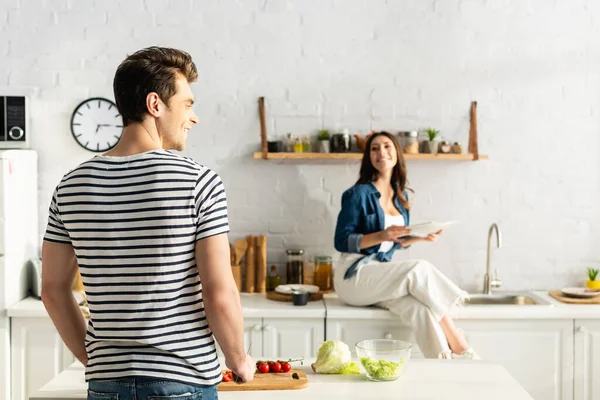 Glücklicher Mann schneidet Kirschtomaten neben Frau auf verschwommenem Hintergrund — Stockfoto