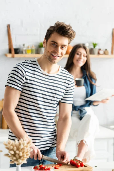 Homem sorrindo perto de mulher segurando copo e jornal no fundo borrado — Fotografia de Stock