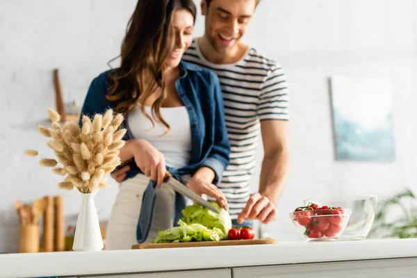 Kätzchen in der Nähe fröhliches Paar bereitet Salat in Küche auf verschwommenem Hintergrund — Stockfoto