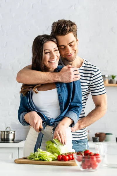 Homme heureux étreignant femme préparant la salade dans la cuisine — Photo de stock