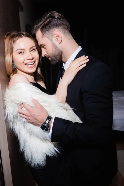 Donna sorridente in soffice giacca abbracciare fidanzato in hotel durante la notte — Foto stock